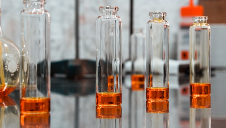 Glass pharmaceutical vials holding amber liquid on a reflective bench