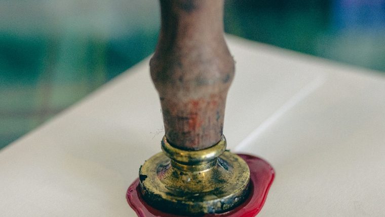 A brass seal pressing red wax onto a sealed envelope