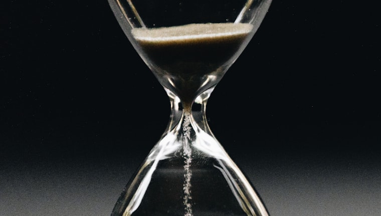Sand running through the neck of an hourglass against a dark background