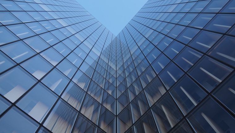 Two modern glass office towers converging upward toward open sky