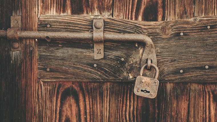 An old padlock hanging from the iron bolt of a weathered wooden door