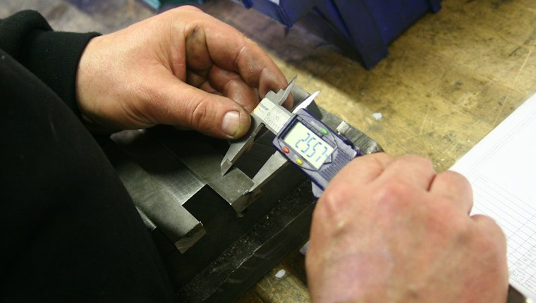 Hands measuring a metal part with a digital caliper